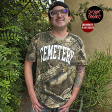 Charger l&#39;image dans la galerie, Man wearing a real tree camouflage t-shirt with &#39;CEMETERY&#39; text, standing outdoors with plants in the background.