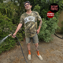 Charger l&#39;image dans la galerie, Man in real tree camouflage &#39;Cemetery&#39; t-shirt holding a hose outdoors with &#39;Discount Cemetery&#39; logo.